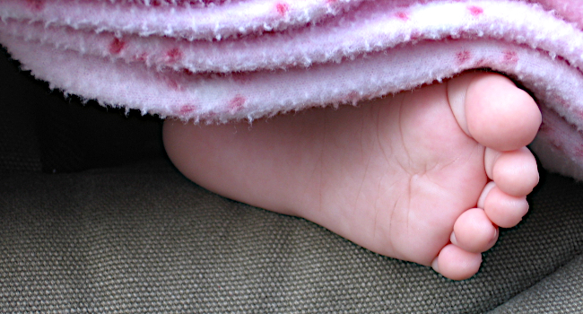 Foto: Kinderfuss unter einer hellrosafarbenen Decke